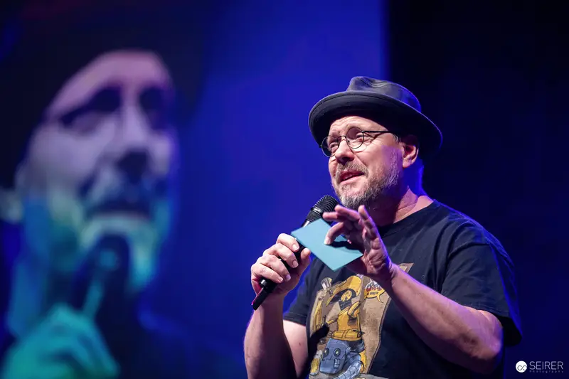 Panel moderator with fedora and microphone on main stage at VIECC Vienna Comic Con 2023
