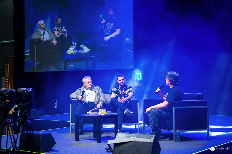 Panel talk with three speakers on blue-lit main stage at VIECC Vienna Comic Con 2023