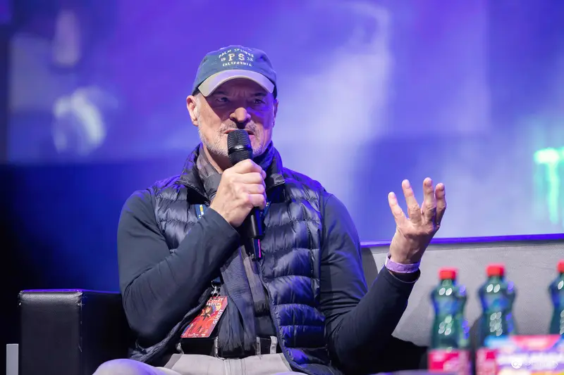 Guest speaker with baseball cap and quilted vest on VIECC Vienna Comic Con panel stage