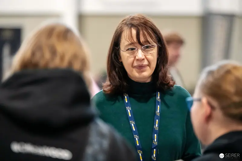 Staff member in green sweater with lanyard talking to visitors at VIECC Vienna Comic Con 2023