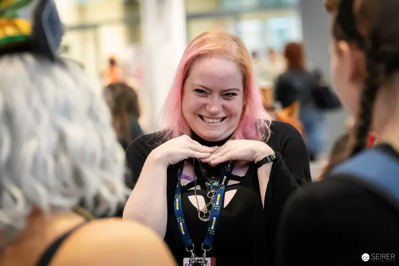 Pink-haired attendee with lanyard laughing in conversation at VIECC Vienna Comic Con 2023