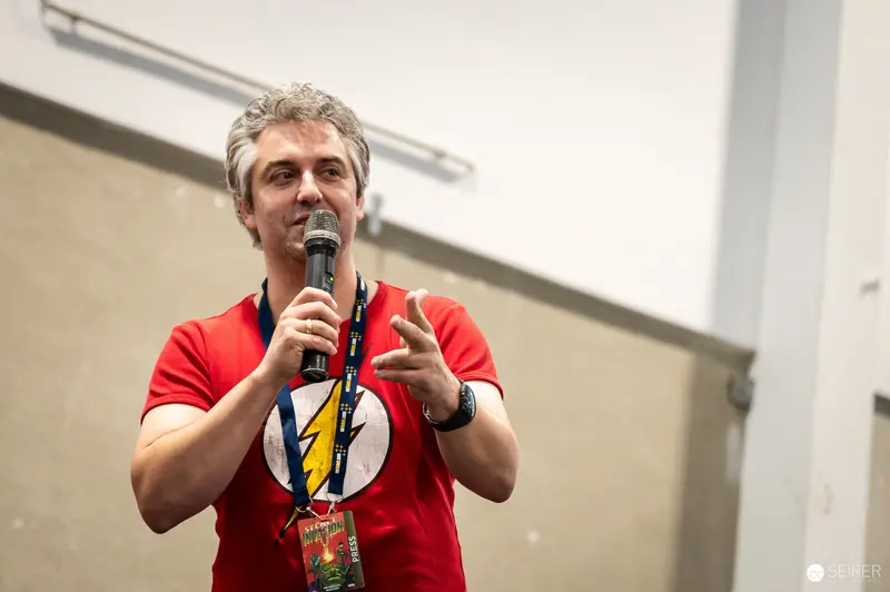 Panel host in red Flash T-shirt speaking into microphone at VIECC Vienna Comic Con 2023