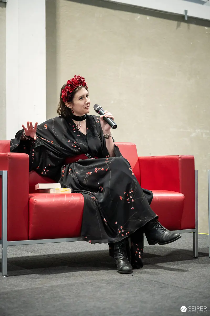 Author with Red Floral Headpiece Speaking on Panel Sofa at VIECC Vienna Comic Con 2023