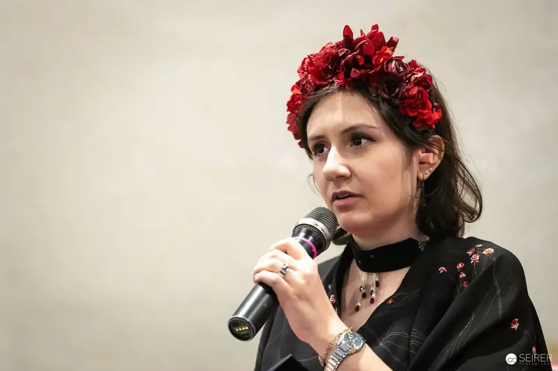 Panel speaker with red floral crown holding microphone at VIECC Vienna Comic Con 2023