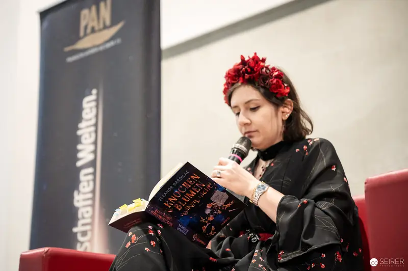 Author reading from Eleanor Bardilac's "Knochen und Blumen" at PAN stage, Vienna Comic Con 2023