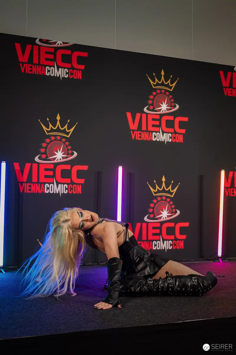 Cosplayer in black leather corset and knee boots poses on VIECC stage backdrop