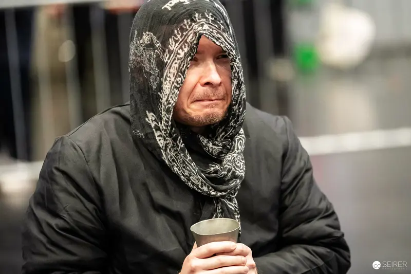 Cosplayer in black hooded robe and patterned headscarf holding metal cup at VIECC 2023
