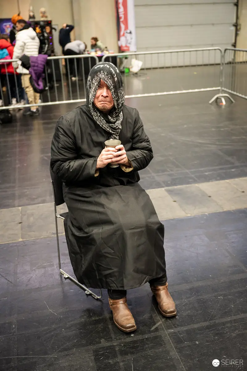 Cosplayer in Black Robe and Patterned Headscarf Resting at VIECC Vienna Comic Con 2023
