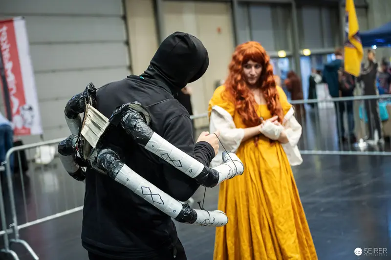 Hooded Cosplayer with Mechanical Arm Rig Meets Golden-Gown Cosplayer at VIECC 2023