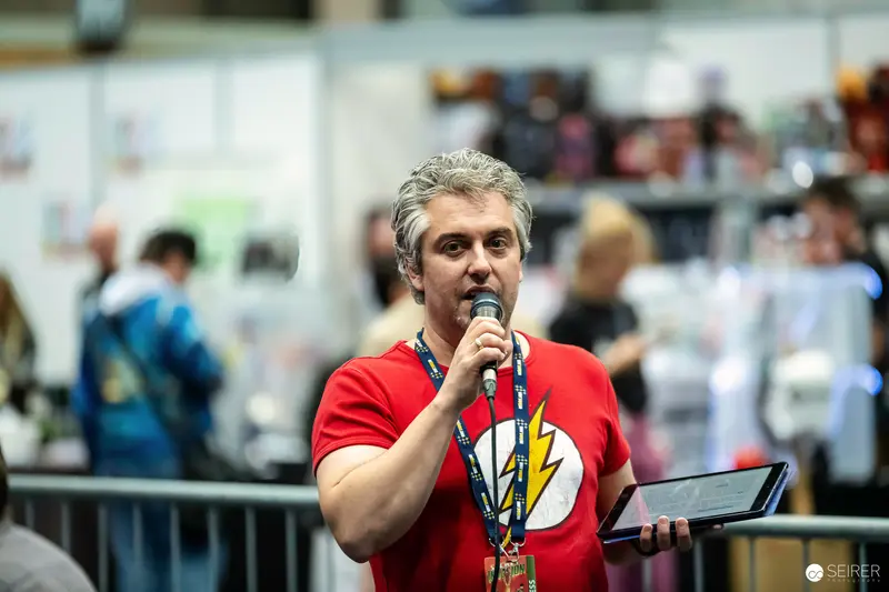 Host with microphone and tablet in Flash T-shirt at VIECC Vienna Comic Con 2023