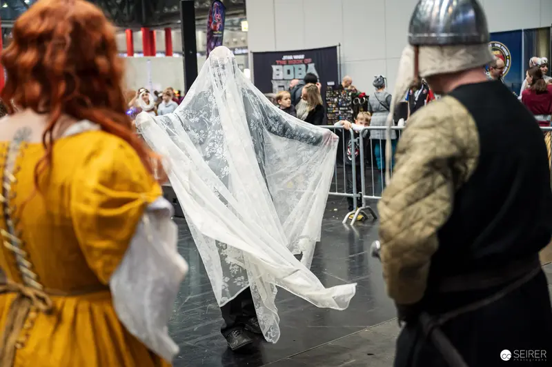 Ghost cosplayer draped in white lace veil between medieval cosplayers at VIECC Vienna Comic Con 2023