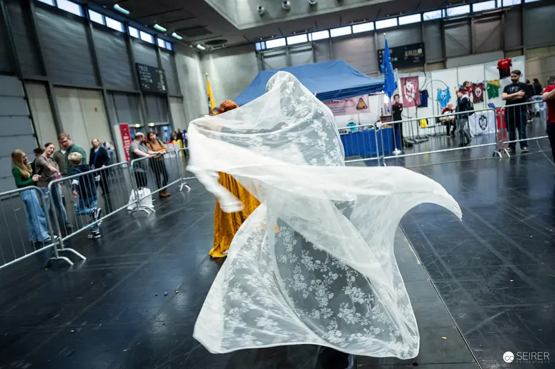 Cosplayer swirling a floral lace veil over a gold costume at VIECC Vienna Comic Con