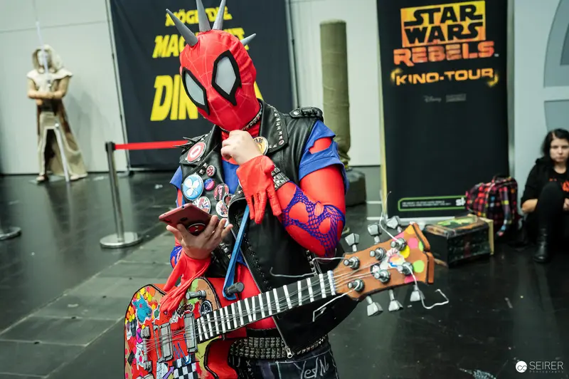 Spider-Punk cosplayer with sticker-covered bass guitar at VIECC Vienna Comic Con 2023