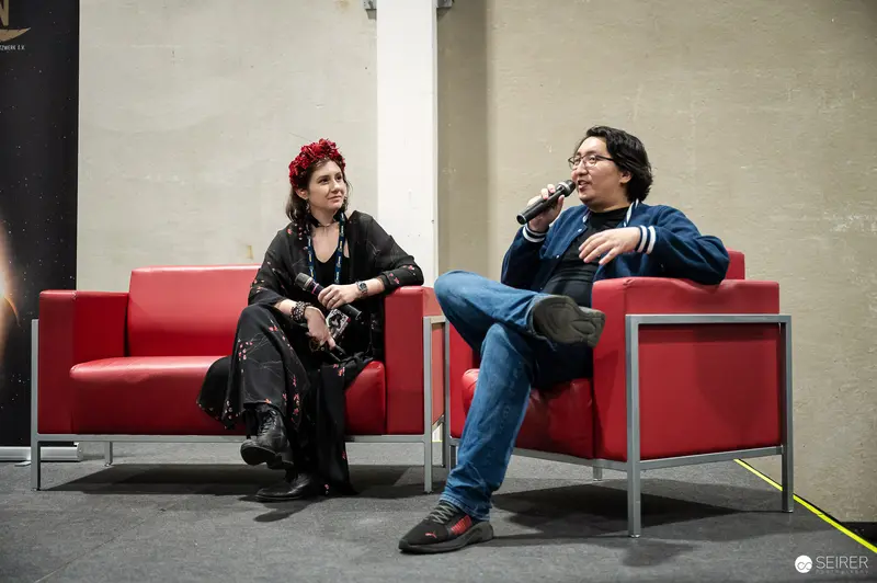 Panel discussion with handheld microphones on red armchairs at VIECC Vienna Comic Con 2023