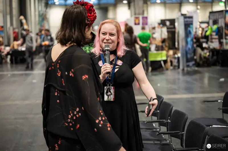 Pink-haired interviewer with microphone speaks to cosplayer at VIECC Vienna Comic Con 2023