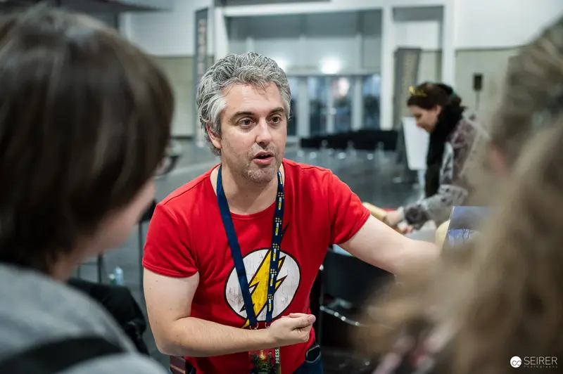 Press-badged staffer in Flash T-shirt talking with visitors at VIECC Vienna Comic Con 2023