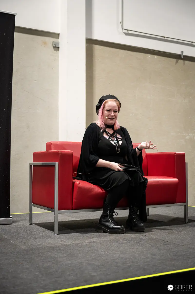 Panel Speaker in Black with Pink Hair on Red Sofa, VIECC Vienna Comic Con 2023