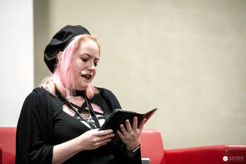 Author with Pink Hair Reads from Notebook at VIECC Vienna Comic Con 2023