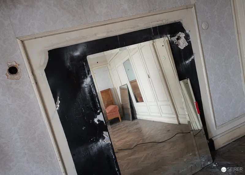 Broken wall mirror reflecting fitted wardrobe in Südbahnhotel Semmering guest room, November 2023