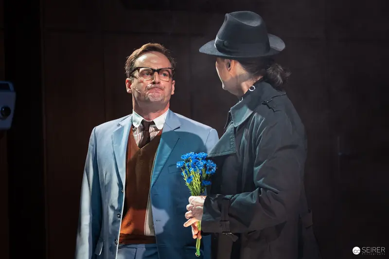 Theater Stage Scene with Two Actors in Blue Suit and Coat, Blue Flowers