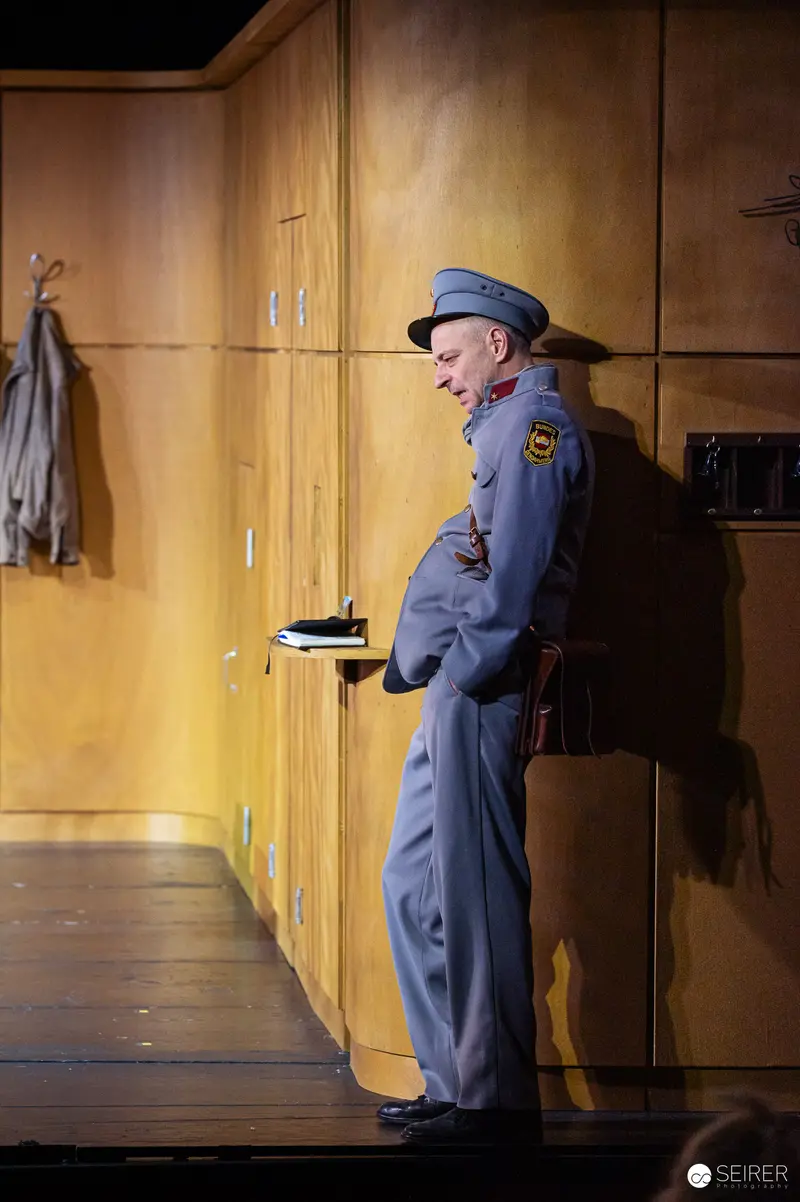Uniformed Officer Pauses by Wooden Lockers in Theatrical Stage Setting