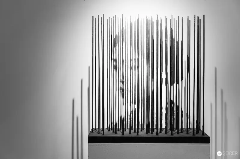 Vertical Linear Sculpture Casting Intricate Shadows on White Gallery Pedestal