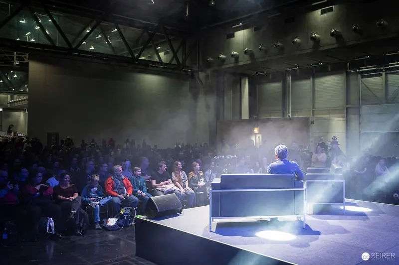 Speaker Presenting on Stage at Vienna ComicCon 2023 Amid Atmospheric Lighting