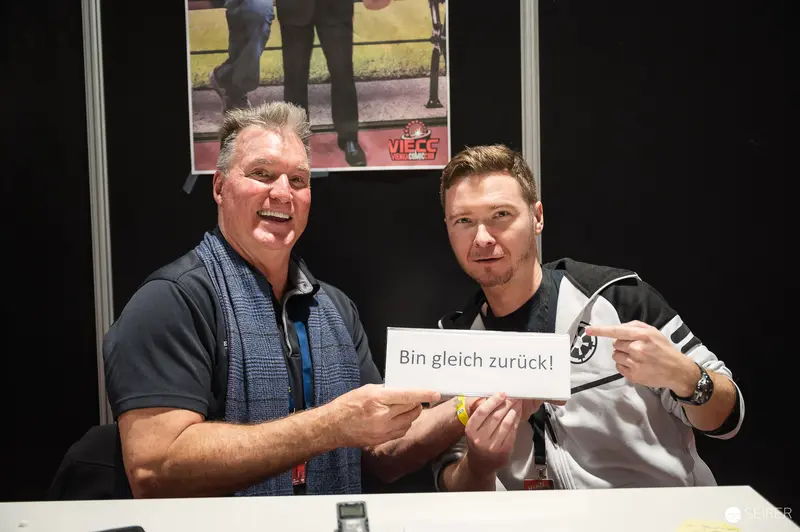 Vienna ComicCon 2023: Two Men Hold "Bin gleich zurück!" Sign