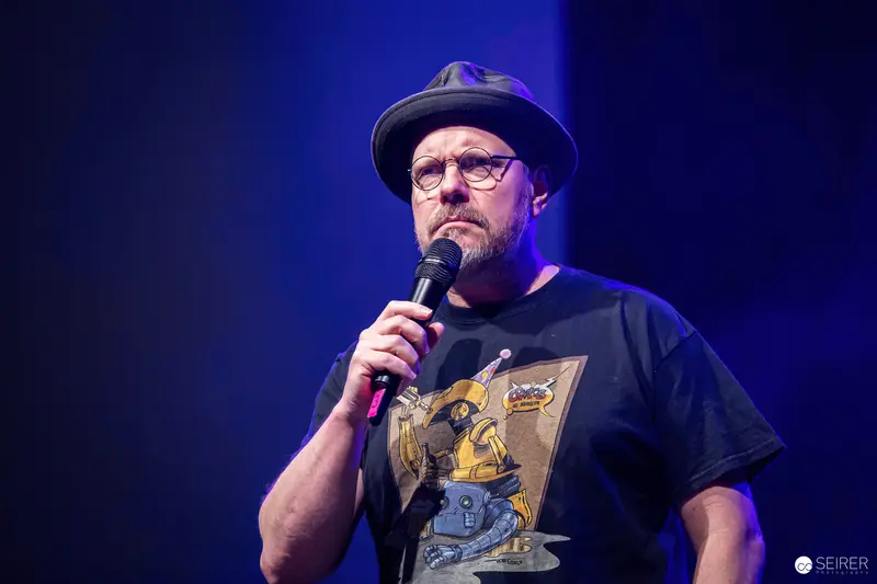 Stand-up Comedian Performing at Vienna ComicCon 2023 in Fedora and Graphic Tee