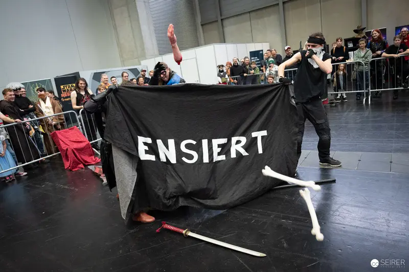Bis Einer Weint Performance Artists with Black 'ENSIERT' Banner at VIECC 2023