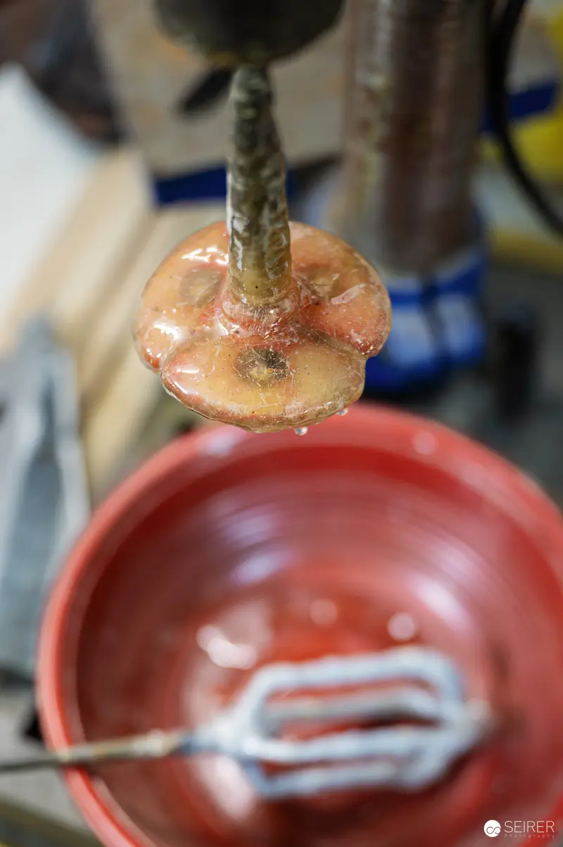 Honey Dripping from Wooden Dipper onto Red Surface in Workshop