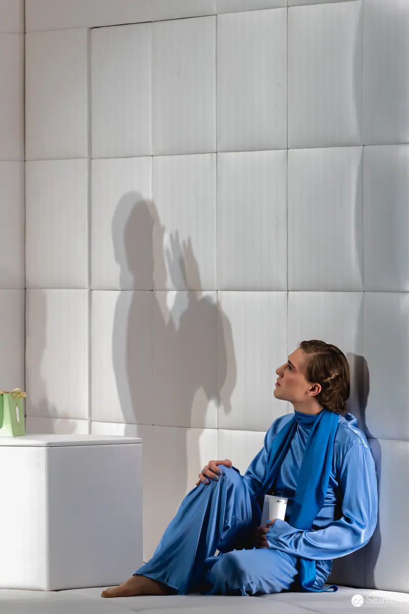 Contemplative Figure in Blue Sitting Against Textured Wall with Shadow