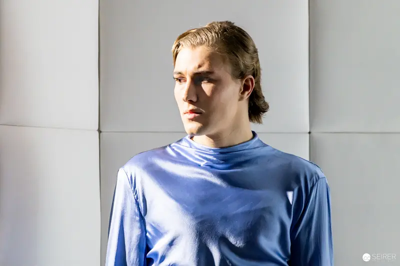 Blue-Clothed Figure in Contemplative Pose Against Textured Wall