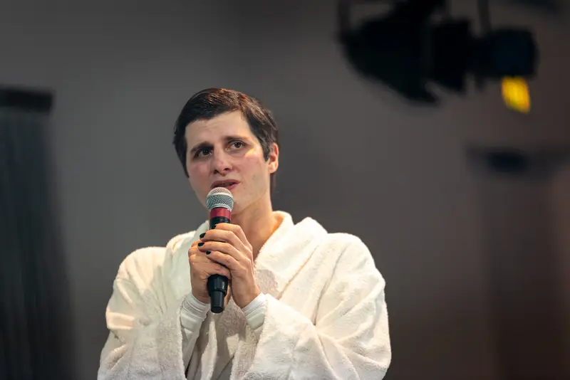 Performer in White Robe Speaking at Kosmos Theater, Wien Performance