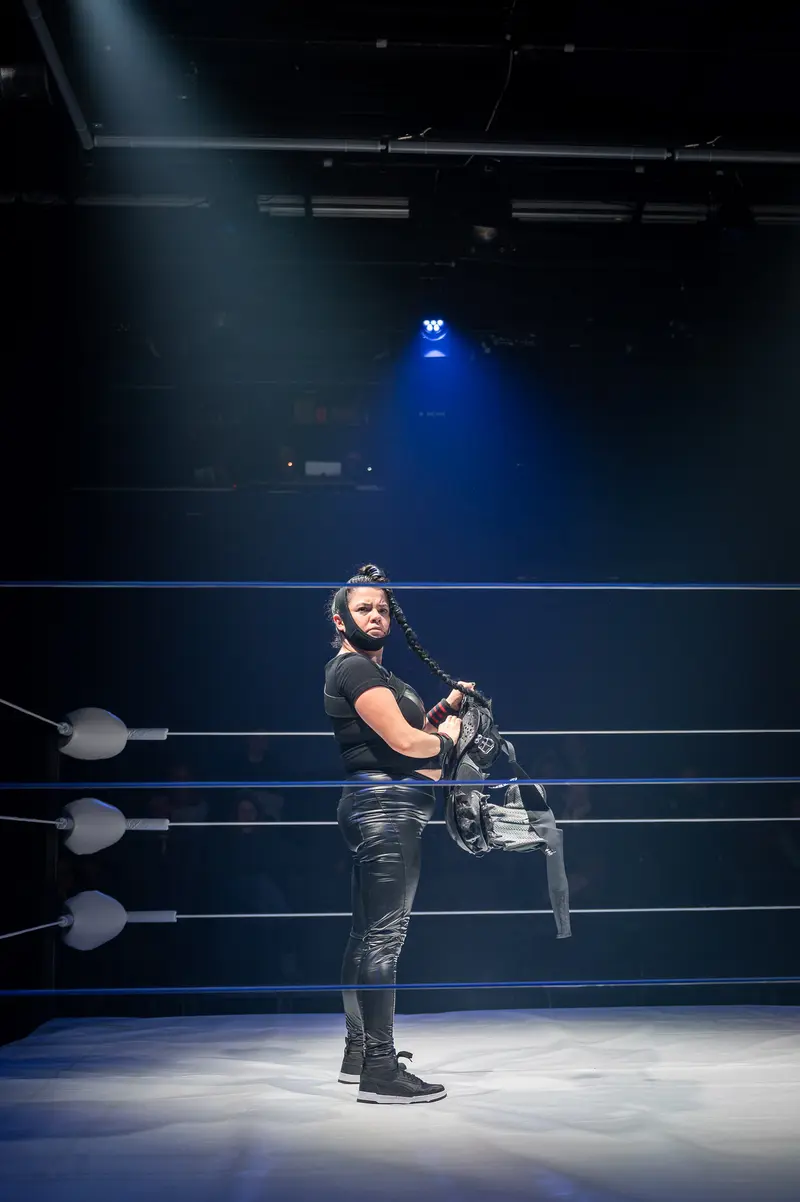 Performer Stands in Dramatic Blue Spotlight at Kosmos Theater Wrestling Production