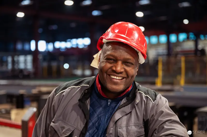 Smiling Industrial Worker in Red Helmet at Frankstahl Manufacturing Facility