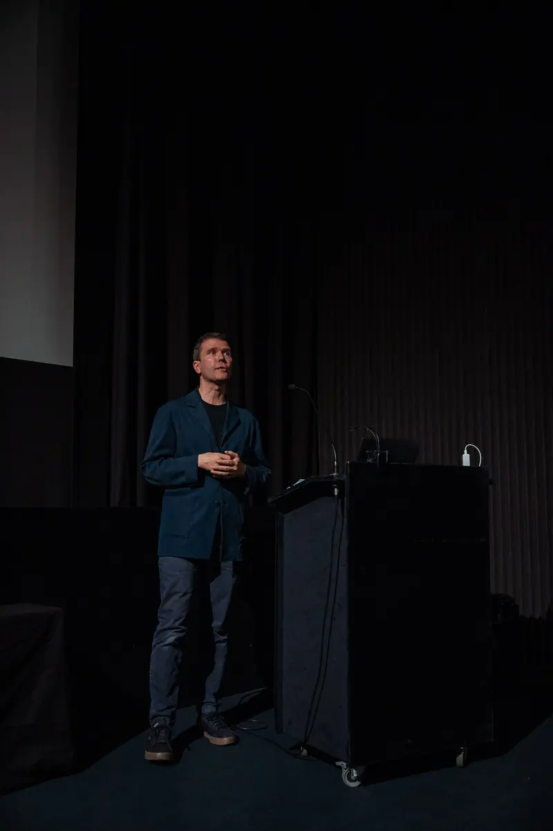 Presenter at 60 Years of Filmmuseum Event Stands Alone on Dark Stage