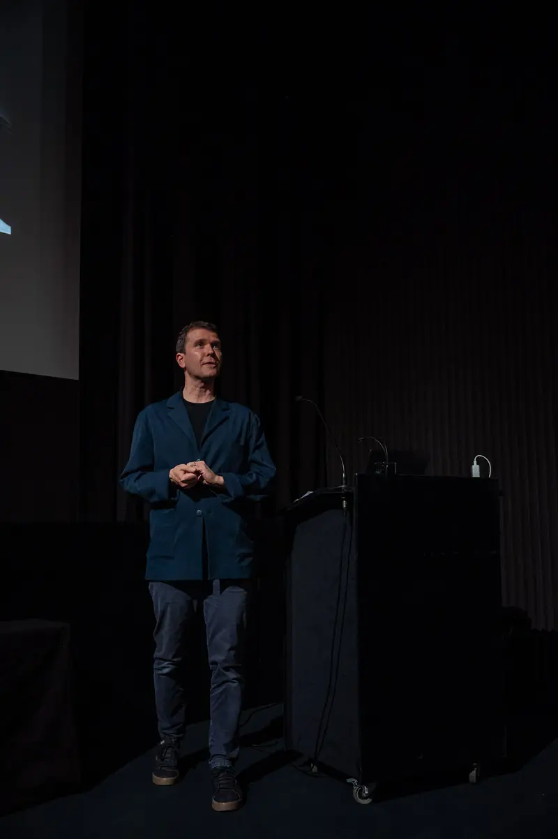 Speaker Presenting at 60 Years of Filmmuseum Event in Dark Stage Setting