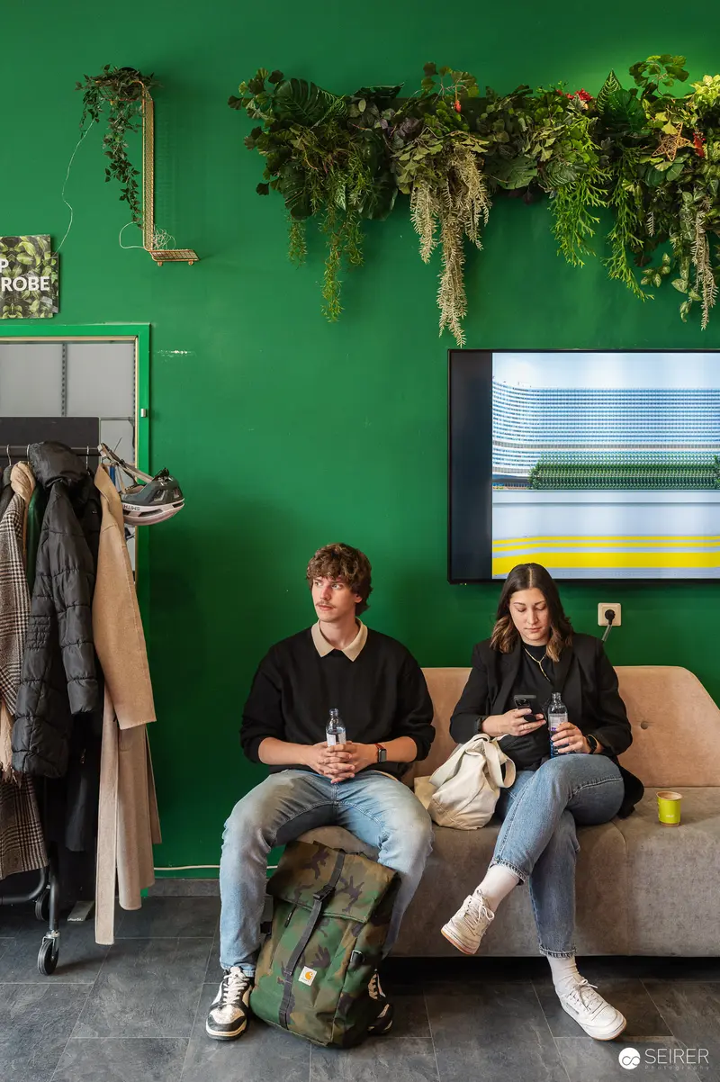 Two Visitors Relax on Beige Couch in Green-Walled Lounge Space