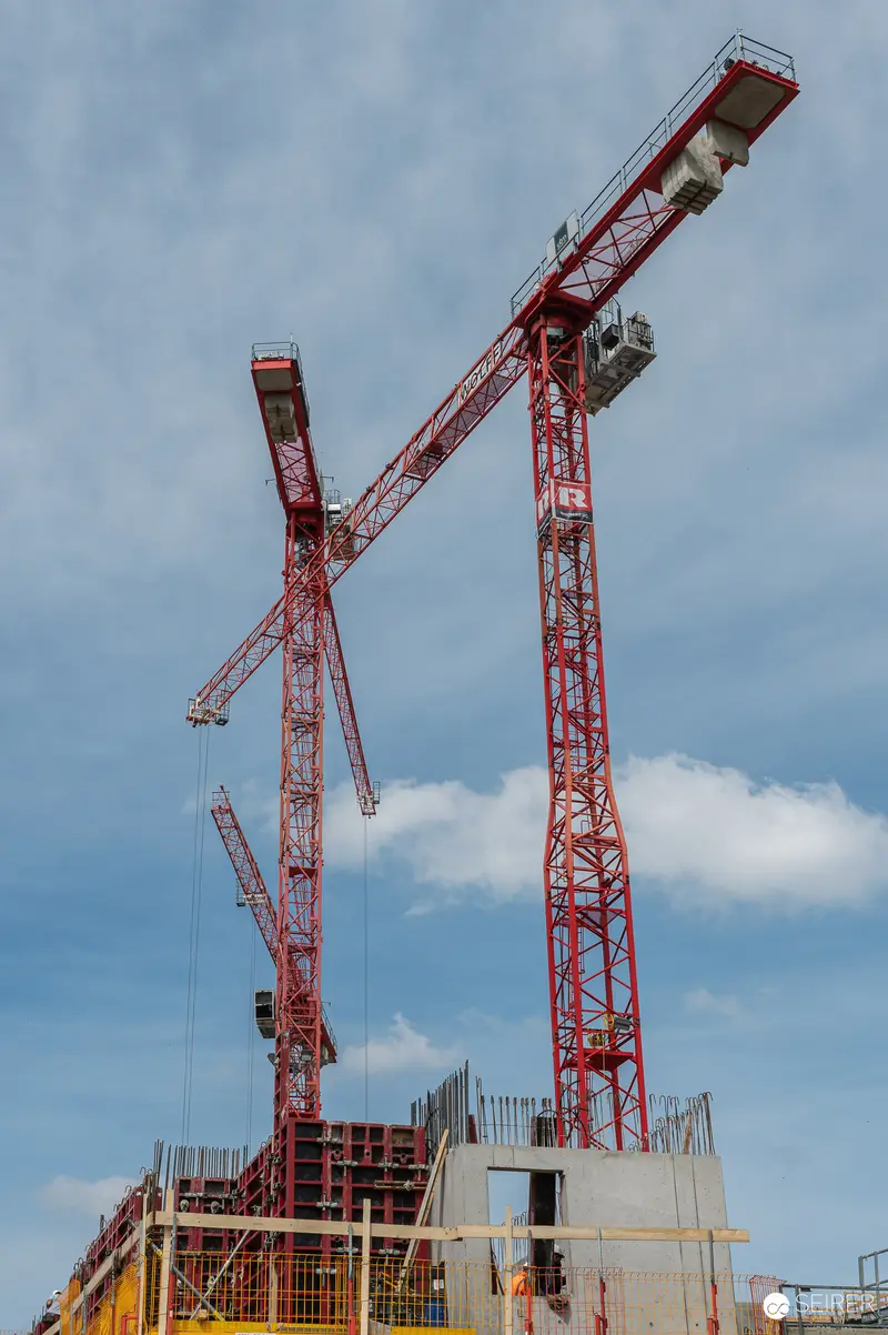 Multiple Red Tower Cranes on Active Construction Site Against Cloudy Sky