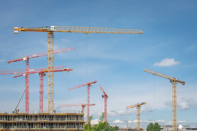 Multiple Construction Cranes at Major Building Site Against Blue Sky