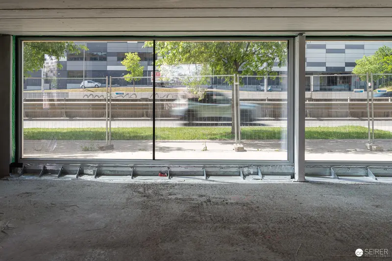 Construction Site Interior with Floor-to-Ceiling Windows Overlooking Urban Neighborhood