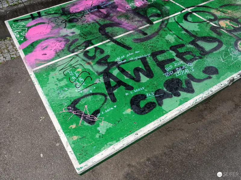 Vandalized Green Street Panel with Graffiti and Pink Spray Paint Markings
