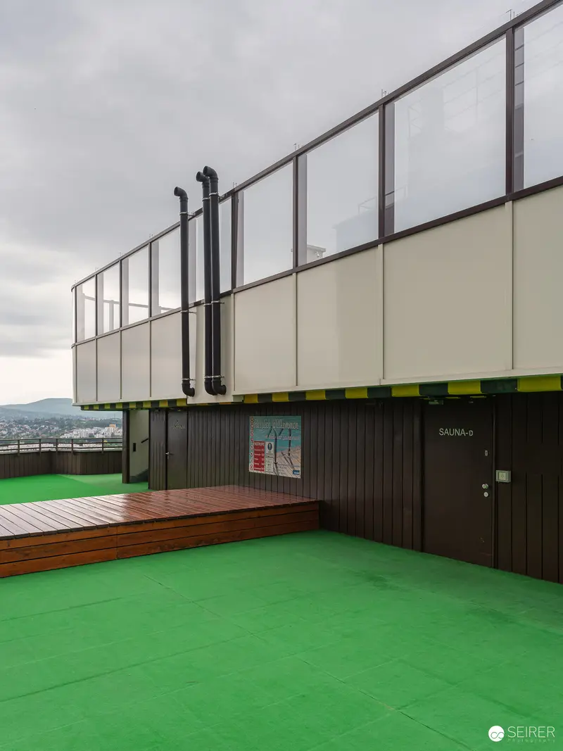 Modern Rooftop Terrace with Green Floor and Steel Railing at Urban Complex