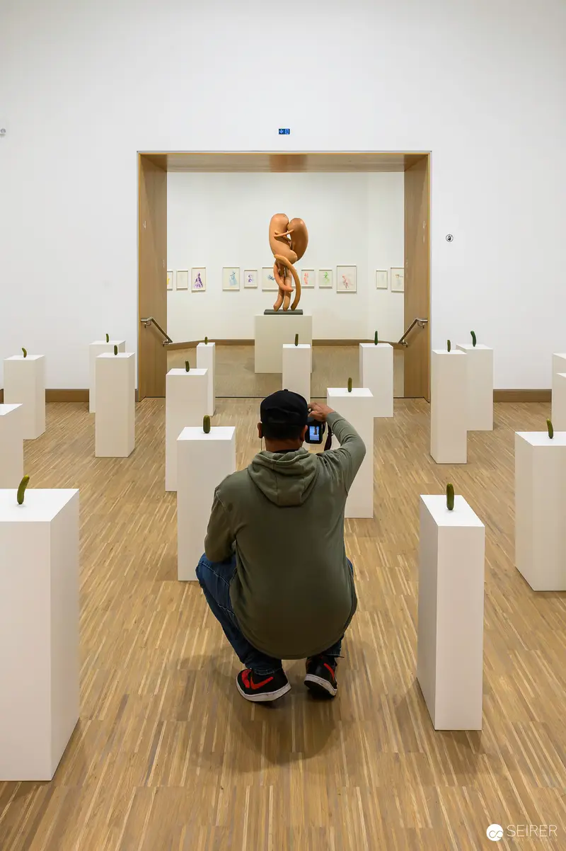 Erwin Wurm Retrospective: Viewer Crouching Among Sculptural Pedestals at ALBERTINA MODERN