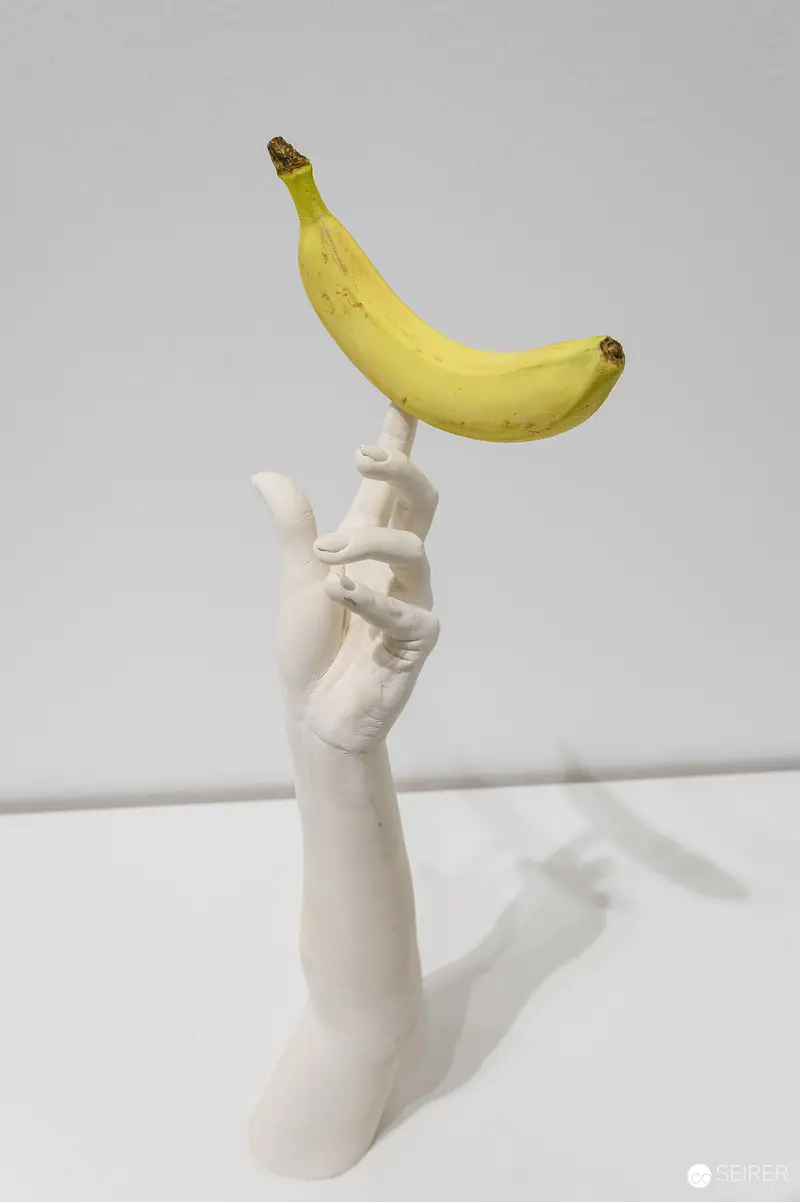 White Sculptural Hand Balancing Ripe Yellow Banana in Surreal Pose