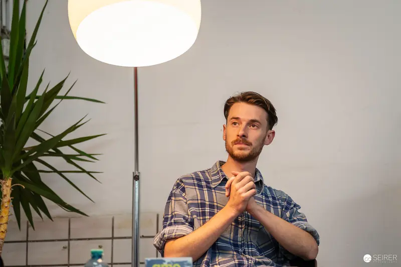 Thoughtful Man in Plaid Shirt at Indoor Event with Floor Lamp