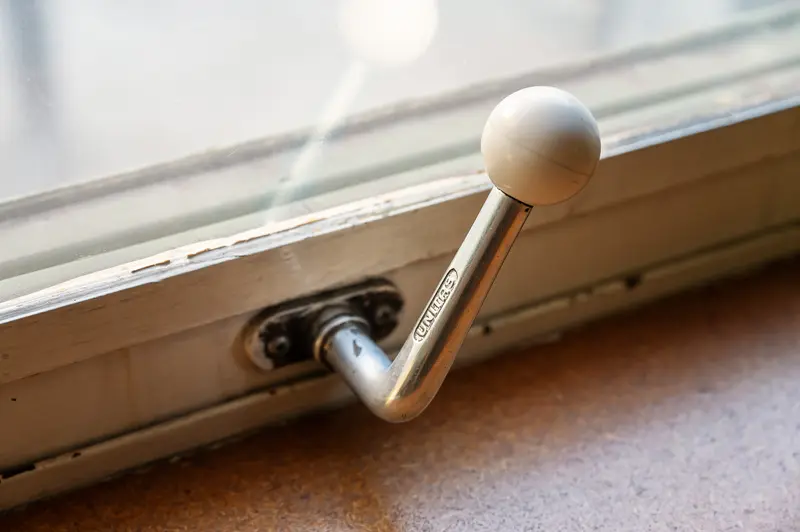 Metal Window Crank Handle with White Spherical Knob on Windowsill