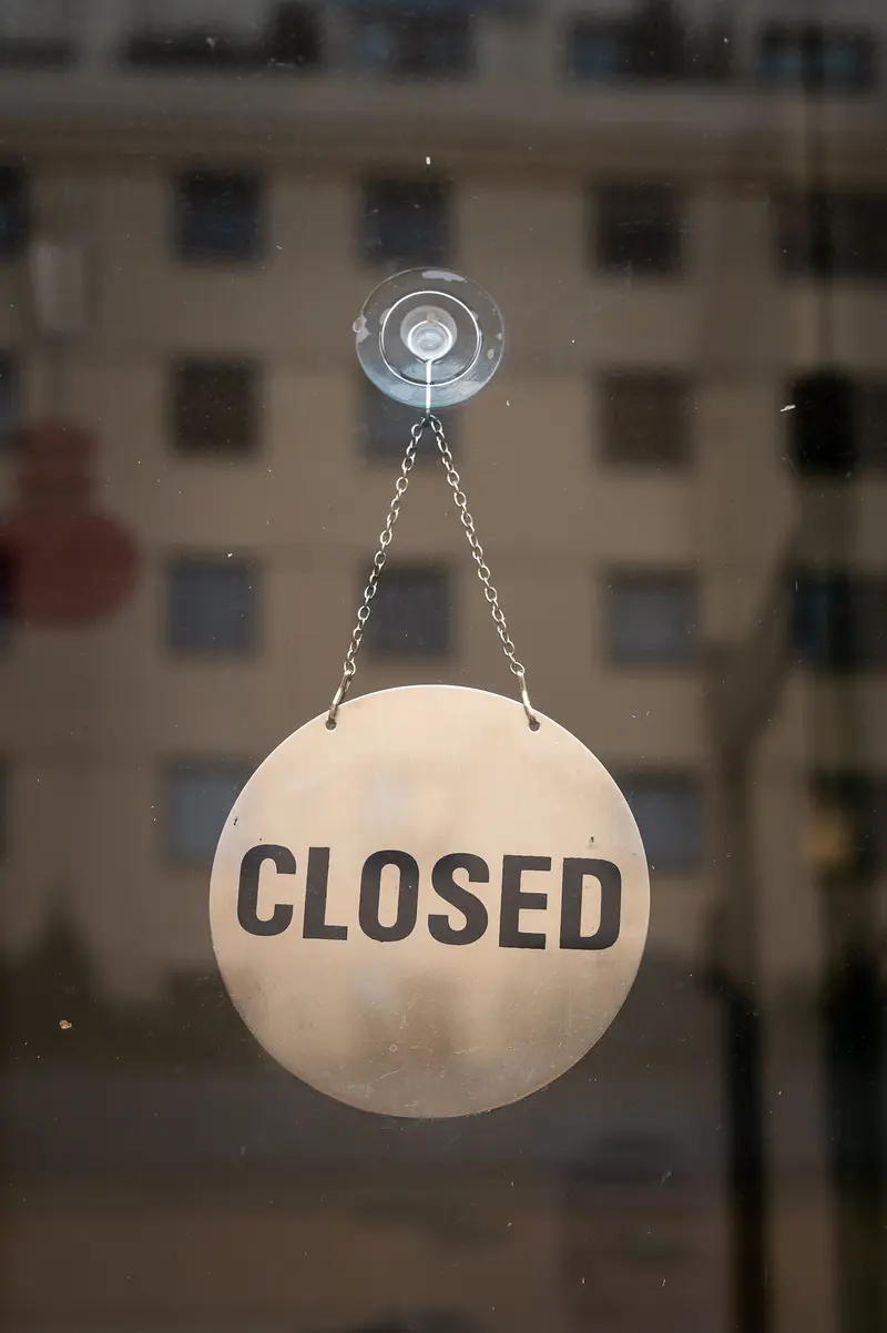 Closed Sign Hanging on Glass Window with Blurred Building Background