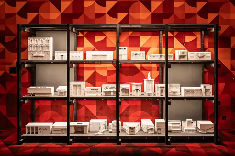 Architectural Model Collection Displayed on Modular Shelving with Geometric Red Background